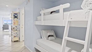 Ein Stockbett mit Kissen und Decke, eine weiße Tür und ein Blick auf einen Balkon mit einem Stuhl.