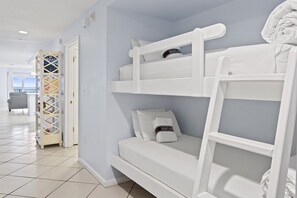 A bunk bed with pillows and a blanket, a white door, and a view of a balcony with a chair.