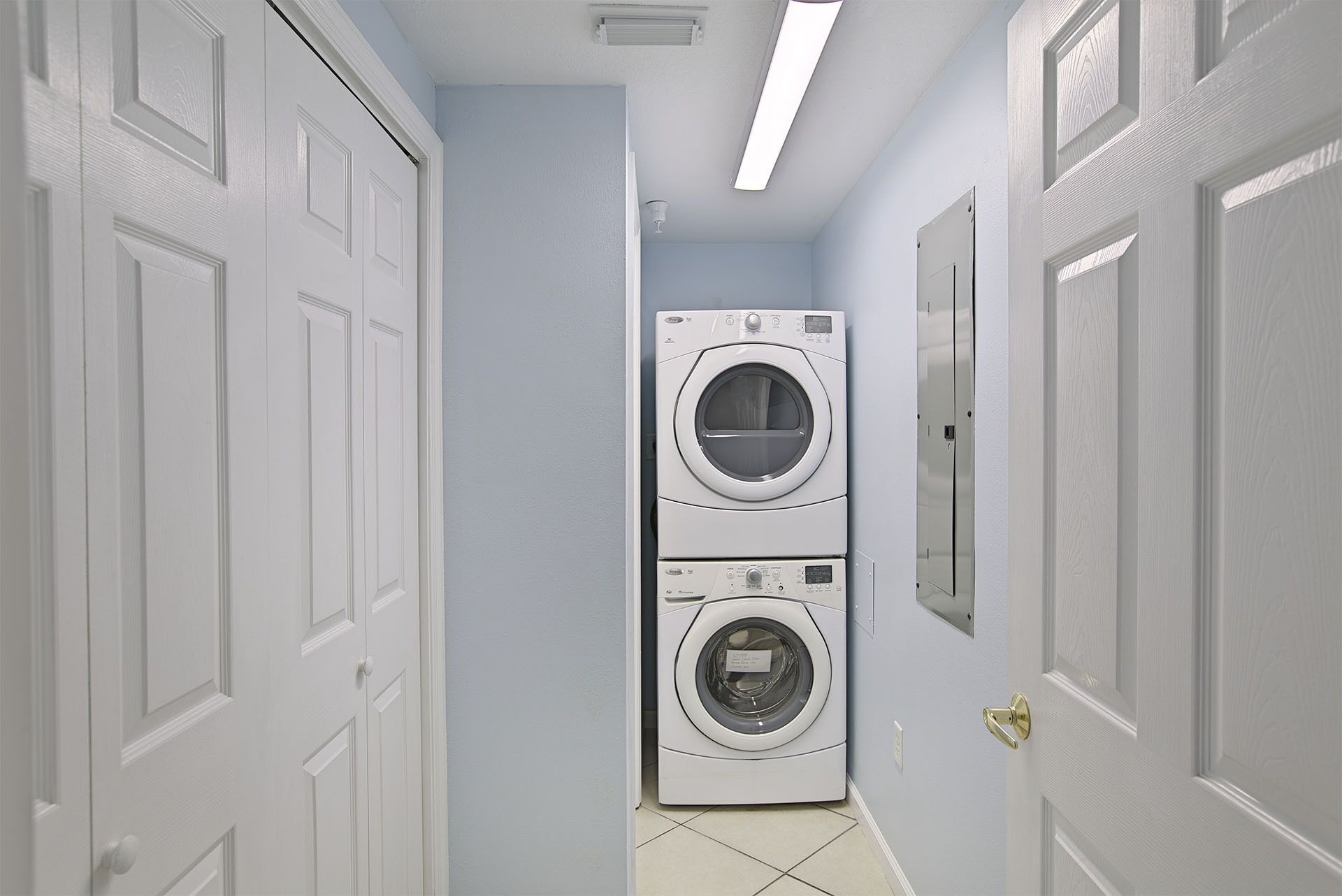 A laundry room with two stacked washing machines, white doors, and a ceiling light.