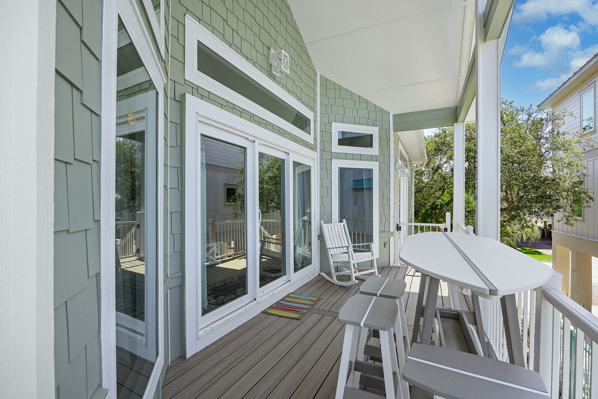 A covered porch with sliding glass doors, a white table, and a white chair.