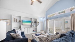 A living room with a TV, white cabinets, a dining table, and a view of the outside. - Hideout – Updated! Pet Friendly & Walk to Beach! (Destin)