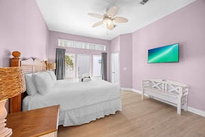 A bedroom with a bed, a television, a ceiling fan, and a view of the outdoors.