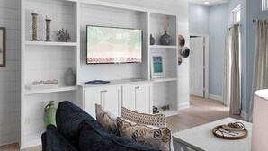 A living room with a flat-screen TV, white shelves with decorative items, a sofa, and a coffee table. - Hideout – Updated! Pet Friendly & Walk to Beach! (Destin)