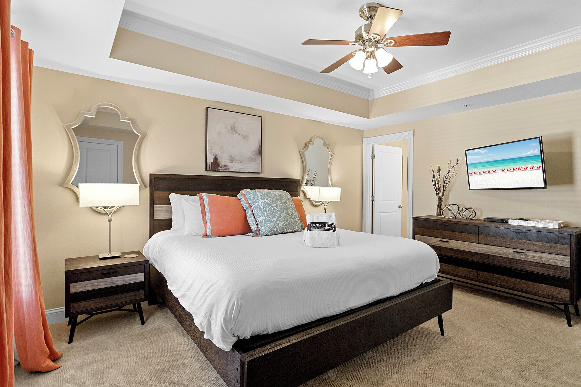 A bedroom with a large bed, a ceiling fan, a TV, and a dresser.