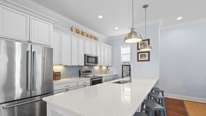 A modern kitchen with white cabinetry, stainless steel appliances, a large island with bar stools, and pendant lighting. - Gone Coastal - Dune Allen Beach! 30A! Community Pool! Steps to the Sand! (Santa Rosa Beach)