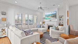 A modern living room with a sectional sofa, a fireplace, and a large TV mounted above it. - Amazing Grace - Destiny West, Heated Private Pool, Fitness, Community Hot Tub! (Destin)