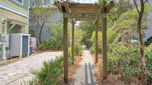 Um arco de madeira com a inscrição 'Beach Access' que dá acesso a um caminho rodeado por vegetação.