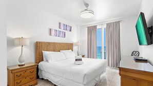 Une chambre d’hôtel avec un lit, deux tables de chevet, une commode, une télévision et une fenêtre avec des rideaux.