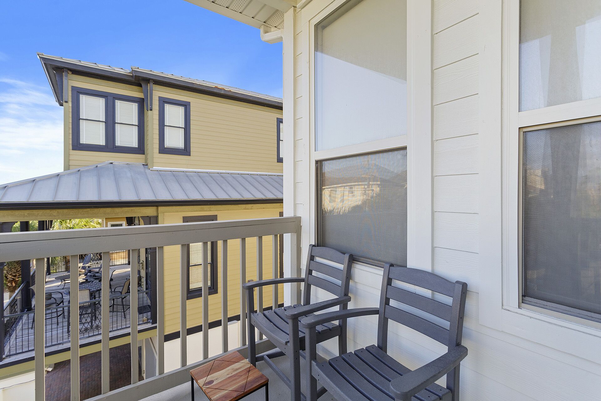 Un balcon avec deux chaises et une petite table, donnant sur un immeuble à la façade jaune et au toit gris.