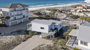 A beachfront property with a multi-story building, a smaller single-story structure, and a sandy beach area with palm trees. - Averitts Favorite - Newly Renovated, Gulf View, Tang-O-Mar Community! (Destin)