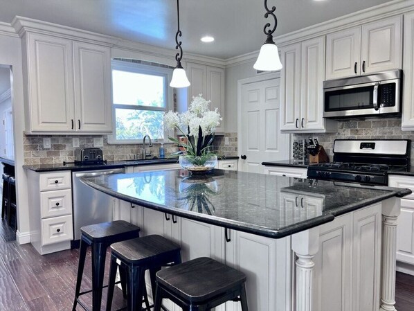 A kitchen with white cabinets, a large island with stools, a microwave, and a stove.