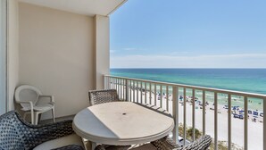 Un balcon avec une table et des chaises, donnant sur une plage parsemée de parasols et fréquentée par des gens.