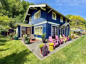 A two-story house with a covered porch, outdoor seating, and a well-maintained lawn. - SHABBY CHIC WATERFRONT RETREAT serene low bank waterfront home w/ gas fire pit. (Vashon)