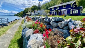 A coastal house with a stone wall and flower beds in front. - SHABBY CHIC WATERFRONT RETREAT serene low bank waterfront home w/ gas fire pit. (Vashon)