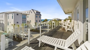 A balcony with white Adirondack chairs, a wooden deck, and a view of a building with multiple windows and a white exterior. - Pelican Place - 30A, Seagrove Beach, Heated Saltwater Pool, Deeded Beach Access! (Santa Rosa Beach)