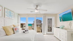 A bedroom with a bed, a nightstand, a dresser, and a ceiling fan. There is a view of the ocean and a house through the glass doors. - Pelican Place - 30A, Seagrove Beach, Heated Saltwater Pool, Deeded Beach Access! (Santa Rosa Beach)