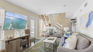 A living room with a TV, sofa, and a staircase leading to an upper level. - Pelican Place - 30A, Seagrove Beach, Heated Saltwater Pool, Deeded Beach Access! (Santa Rosa Beach)