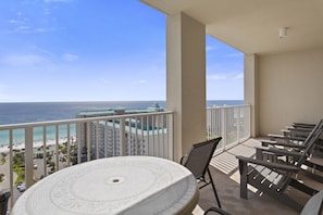 A balcony with a round table and chairs, overlooking a beach and ocean.