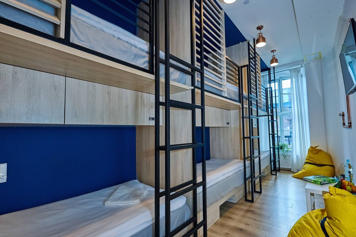 A modern room with bunk beds, a small table with a bottle and fruit, and a window with curtains.