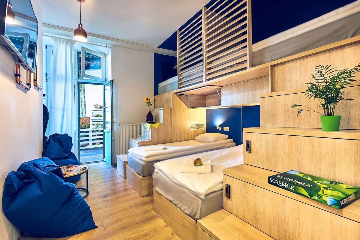 A modern bedroom with two beds, a wooden headboard, a green plant, and a Scrabble game box.
