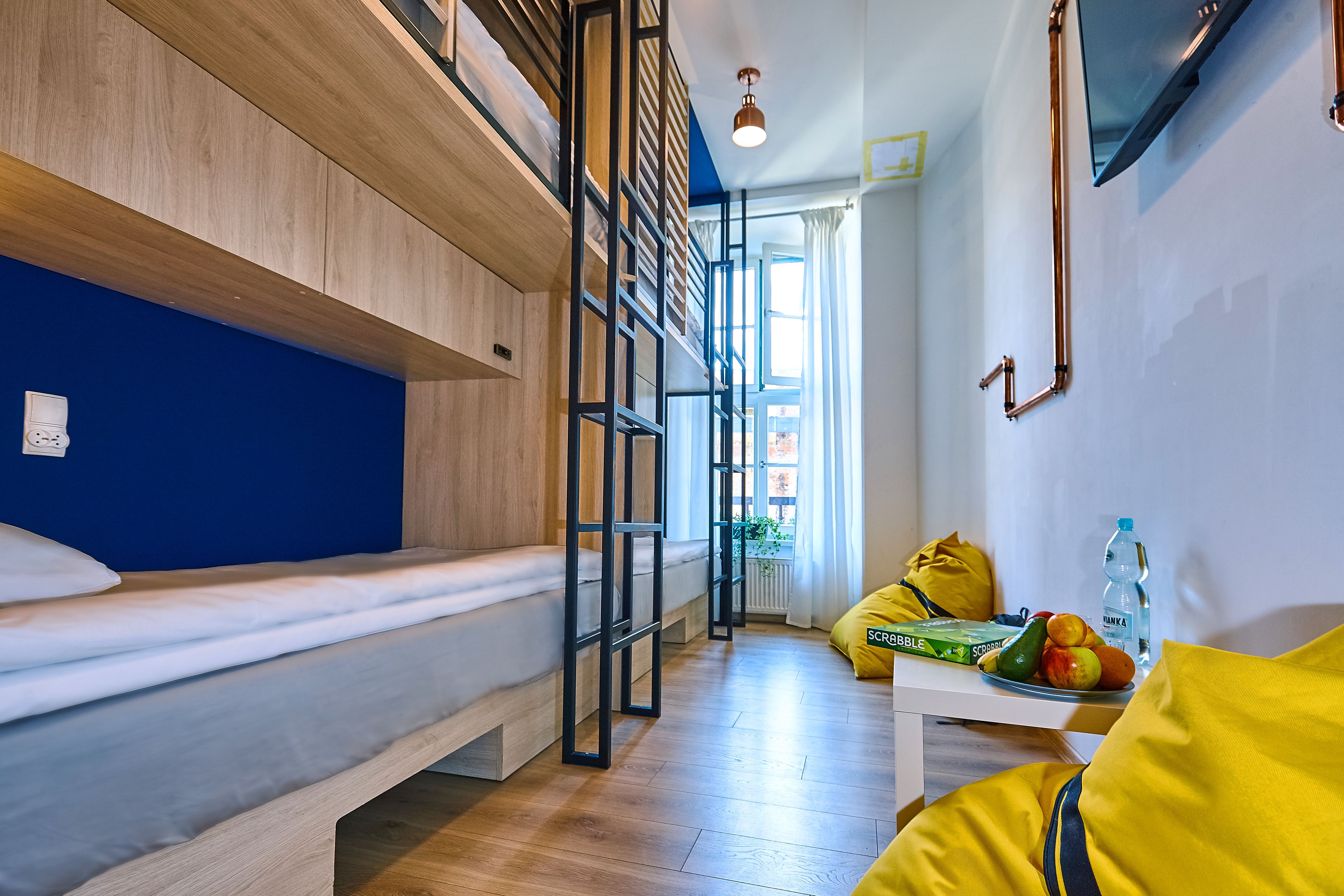 A room with a bunk bed, a desk with a fruit bowl, and a window with curtains.