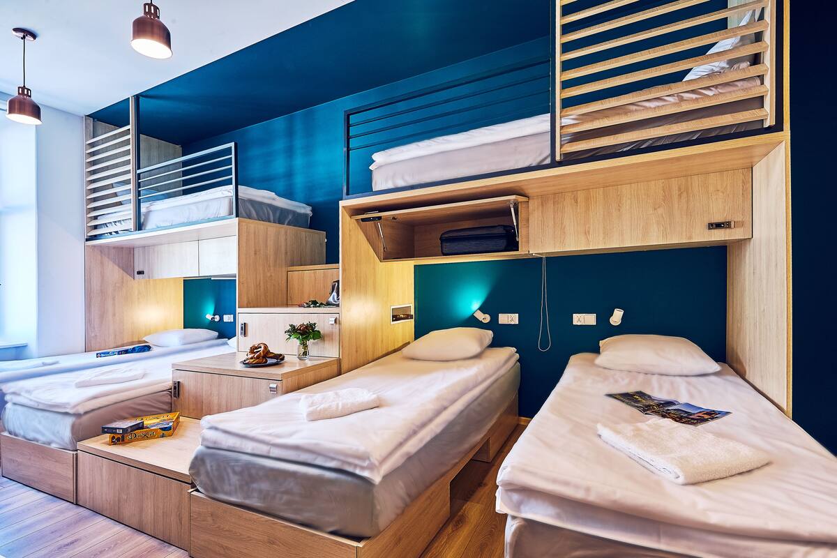 A modern hotel room with two single beds, a bunk bed, and a wooden desk.