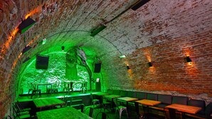 An interior with brick walls, green lighting, tables, and chairs arranged for dining. - Draggo House- Hostel (Kraków)
