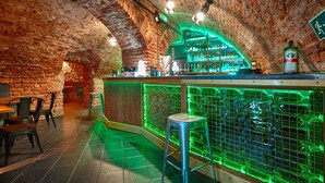 A bar with a brick interior, green lighting, and a stool. - Draggo House- Hostel (Kraków)