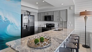 A modern kitchen with a granite countertop, stainless steel appliances, and a large island with stools. - Majestic Sun 208B - Upscale Unit, Gulf Views, Community Pool + Hot Tub! (Miramar Beach)