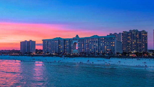 A large hotel with multiple floors and a central courtyard, located near a beach with people on the sand and water. - Majestic Sun 208B - Upscale Unit, Gulf Views, Community Pool + Hot Tub! (Miramar Beach)