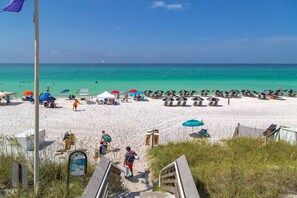Ein Strand mit weißem Sand, klarem türkisblauem Wasser und mehreren Strandsonnenschirmen.