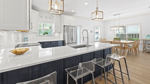 A modern kitchen with a large island, stainless steel appliances, and clear bar stools. - Treasure Chest – Stylish Update, Heated Pool, No Roads to Beach + Outdoor Bar! (Miramar Beach)