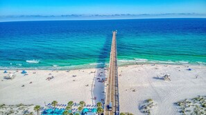 A beach with a long pier extending into the ocean, numerous sun loungers, and clear blue waters.