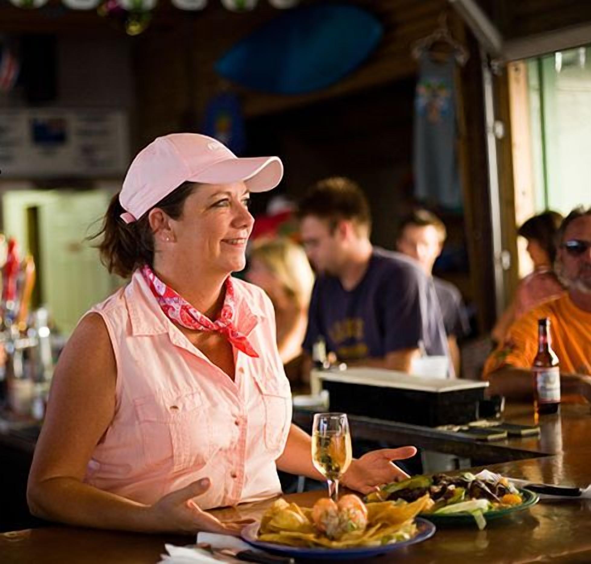 Eine Frau sitzt an einem Tisch in einem Restaurant mit Schild, das Live-Musik und eine Strandlage anzeigt.