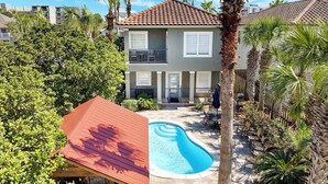 Una casa de dos pisos con piscina, rodeada de palmeras y un patio cubierto.