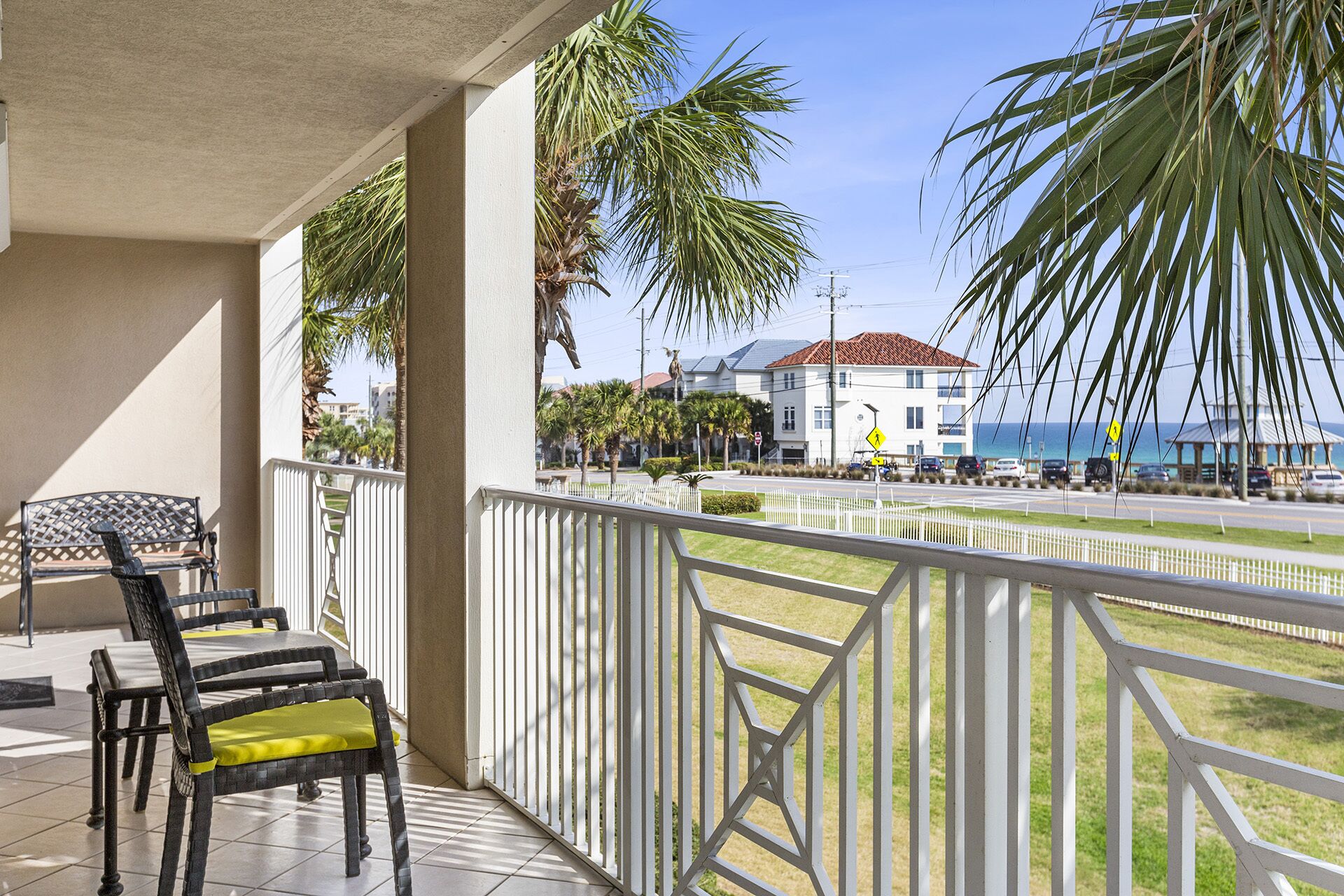 A balcony with two chairs and a table, overlooking a street with palm trees and buildings.
