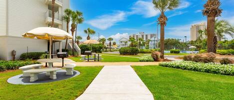 A landscaped outdoor area with a concrete pathway, outdoor seating, and palm trees.