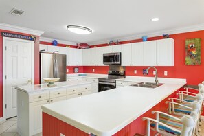 A modern kitchen with white cabinets, stainless steel appliances, and a red accent wall. - Amalfi Coast 201A - Miramar Beach! Gulf Views! Two Pools! Gym! Tennis Courts! (Miramar Beach)