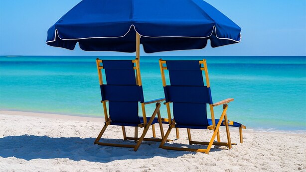 To strandstole under en blå parasol på en sandstrand med klart turkis vand.