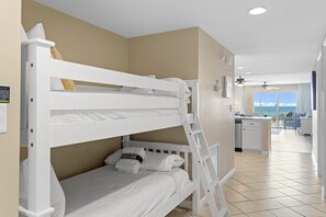 Un lit superposé avec une tête de lit et un pied de lit blancs, une petite table de chevet et une serviette portant la marque « OCEAN REEF ».
