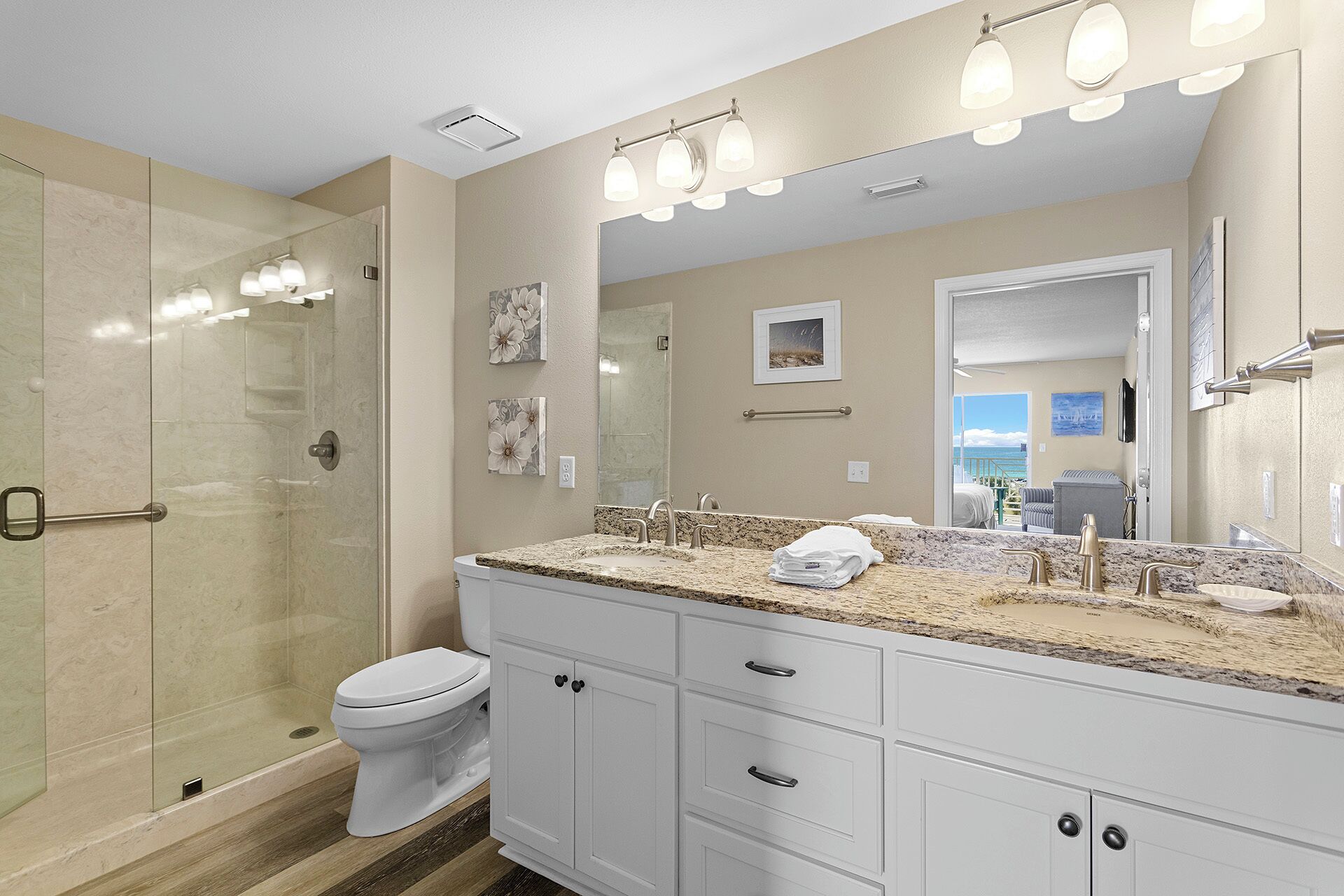 Un baño moderno con cabina de ducha de vidrio, inodoro blanco y tocador con espejo grande.