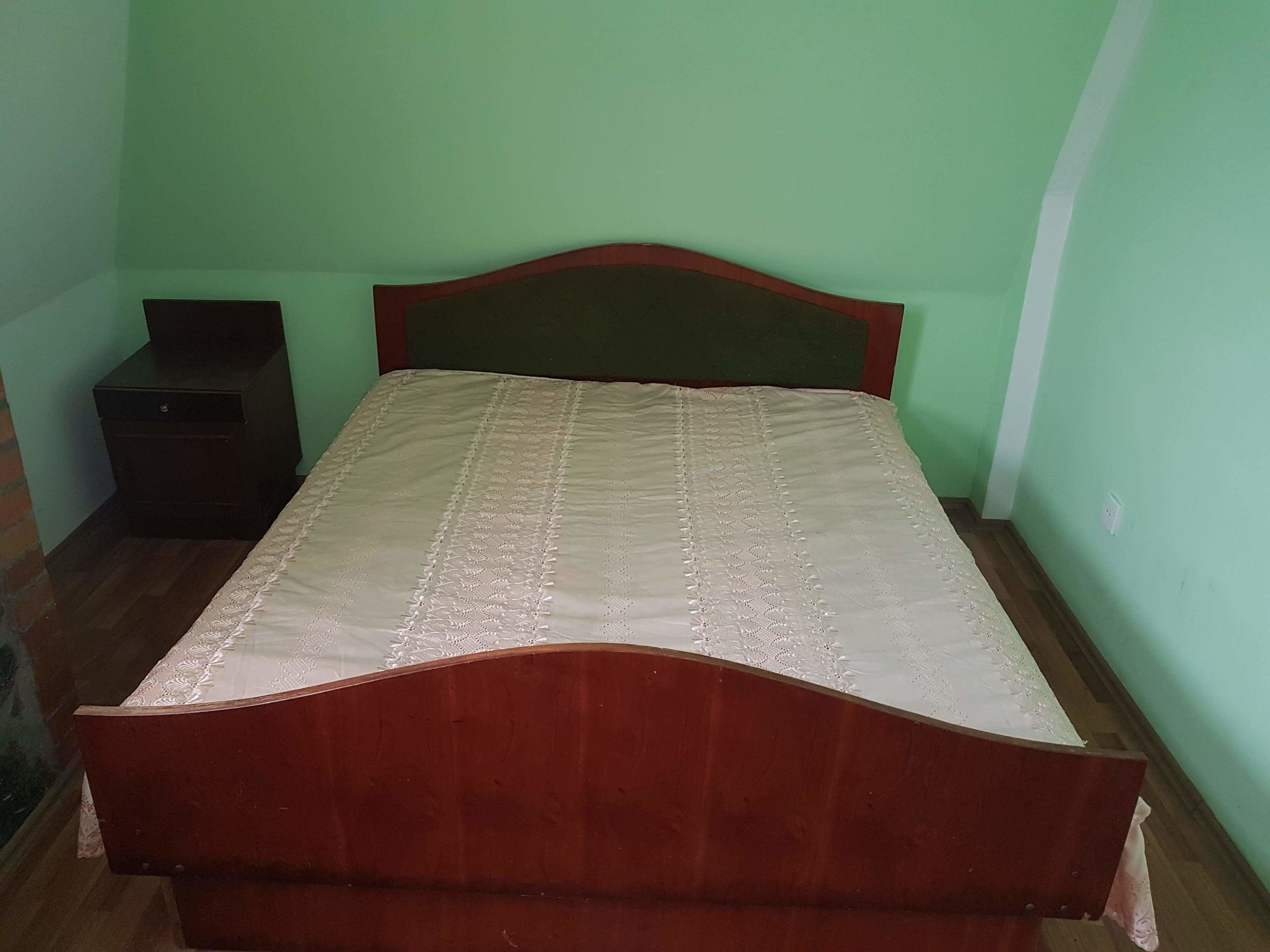 A single-bed room with a wooden headboard, a small bedside table, and a green wall.