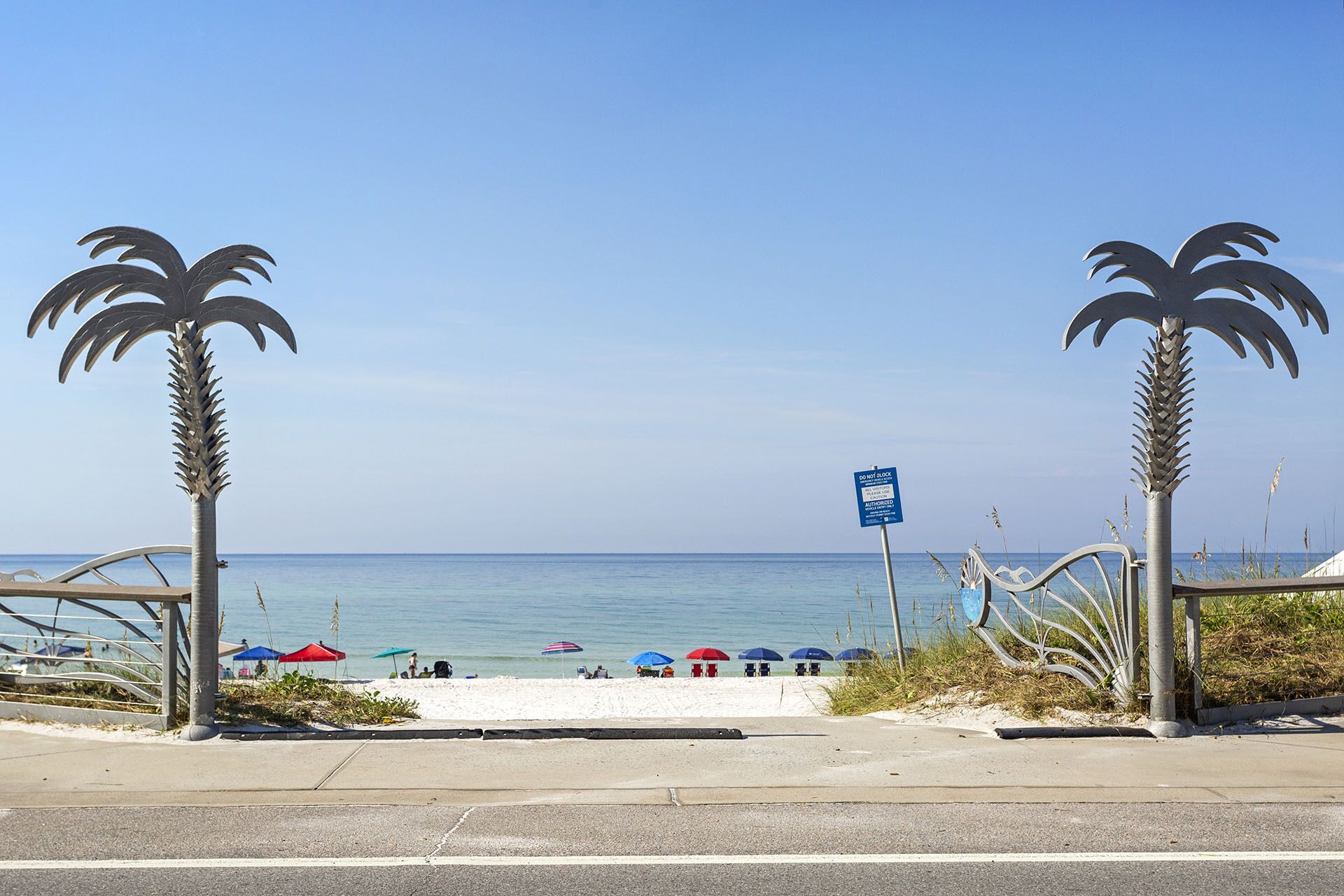 Una spiaggia con palme, un cartello blu e ombrelloni.