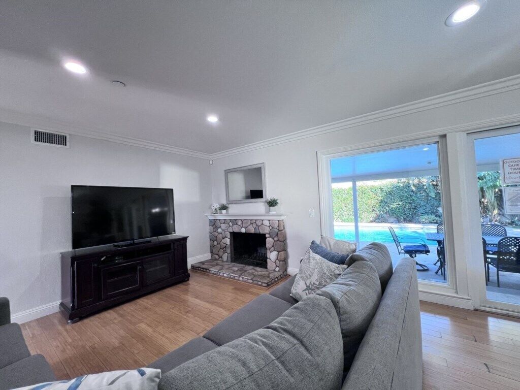 A living room with a TV, fireplace, and a large window overlooking a pool.