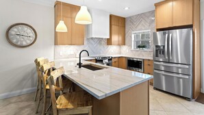 A modern kitchen with wooden cabinets, a marble island, stainless steel appliances, pendant lighting, and a herringbone-patterned backsplash. - Breakaway (Updated) - Steps to the Beach! Private Pool! Great Outdoor Space! (Miramar Beach)