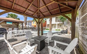 Eine überdachte Terrasse im Freien mit Grill, weißen Adirondack-Stühlen und einem Pool.