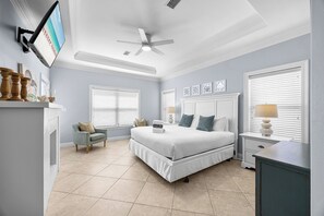 A bedroom with a bed, a chair, a desk, a ceiling fan, and a TV on the wall.
