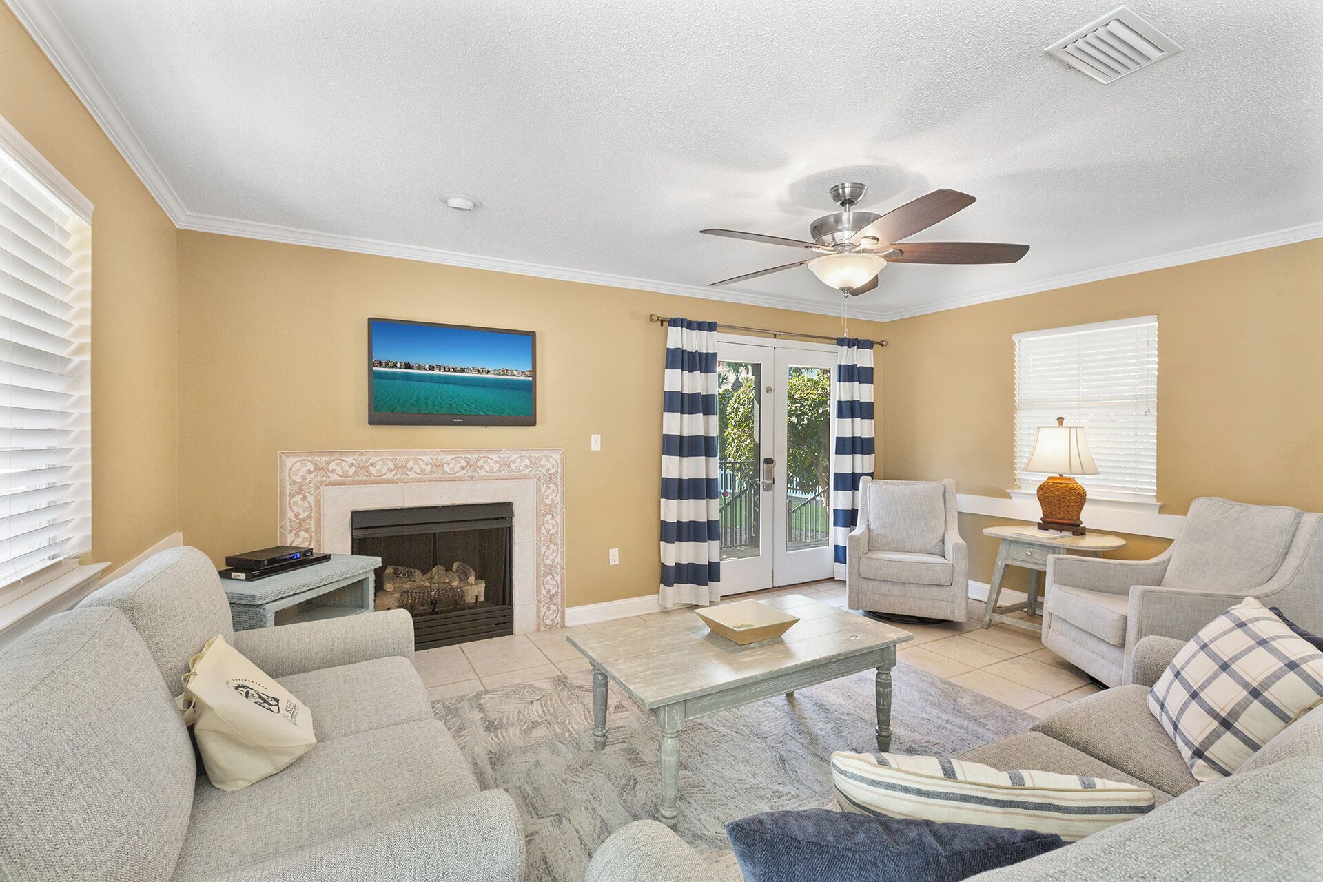 A living room with a fireplace, a ceiling fan, a television, and a view of the outdoors through a glass door.