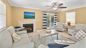 A living room with a fireplace, a ceiling fan, a television, and a view of the outdoors through a glass door. - Panorama - Gulf Views! Heated Private and Community Pool! Free Beach Service! (Miramar Beach)
