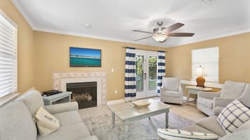 A living room with a fireplace, a ceiling fan, a television, and a view of the outdoors through a glass door.